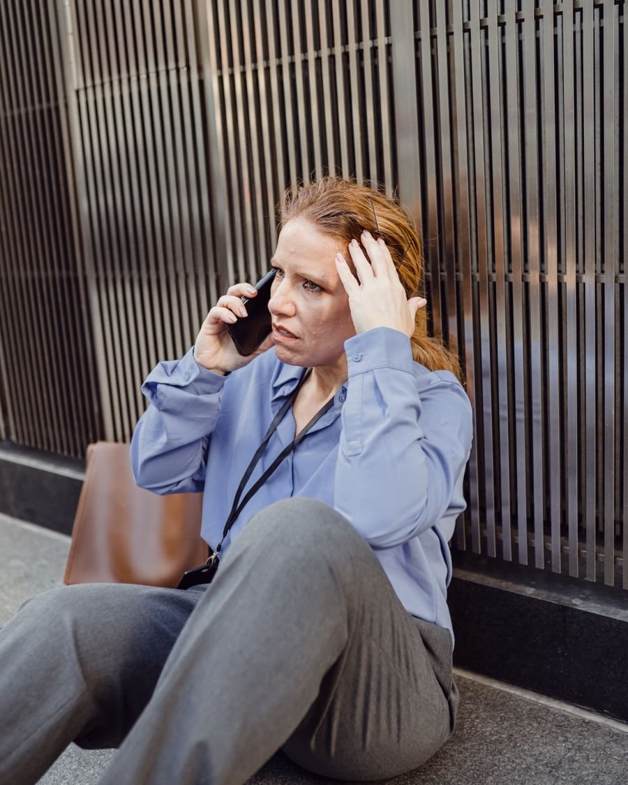 Mulher sentada na calçada, ao telefone, preocupada