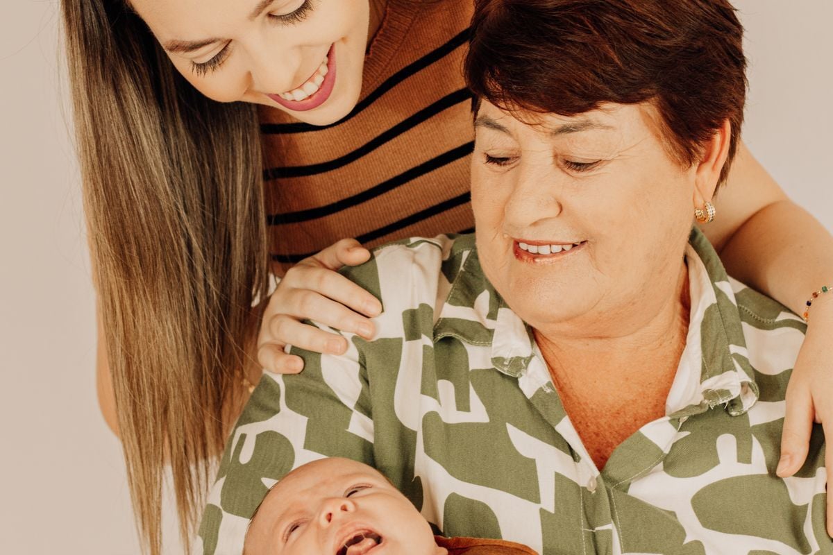 Três gerações de uma família sorrindo juntas, com um bebê no colo