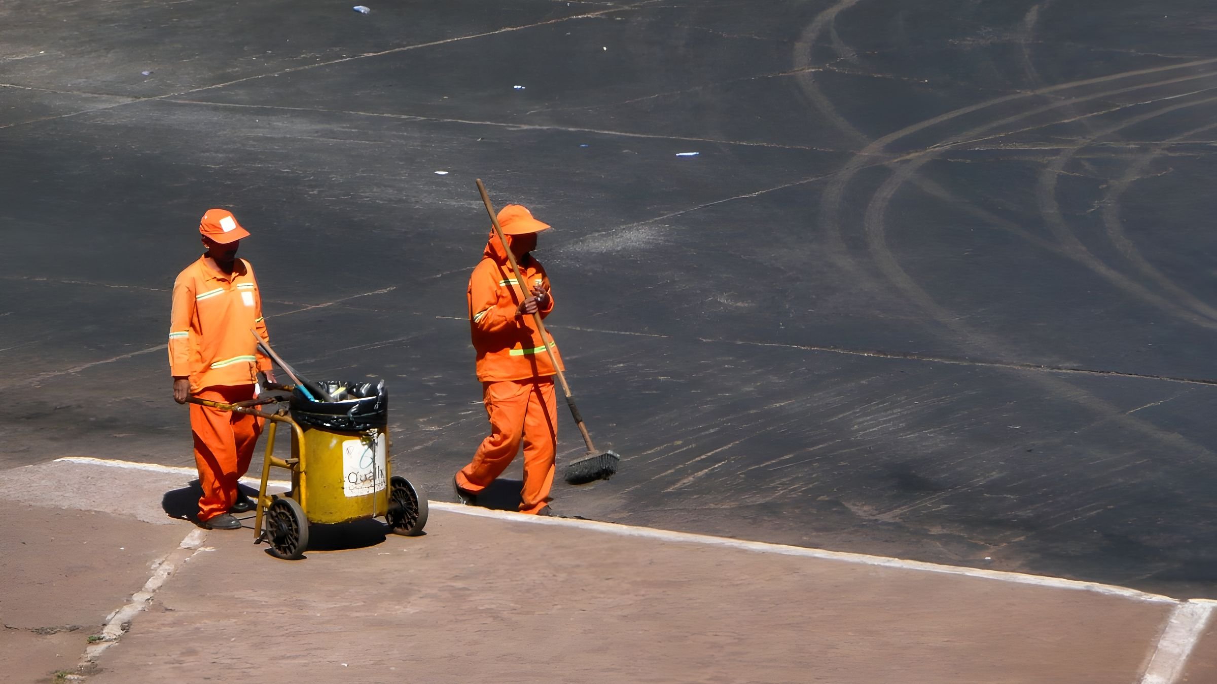 Dois garis de uniforme laranja trabalhando numa rua de Brasília