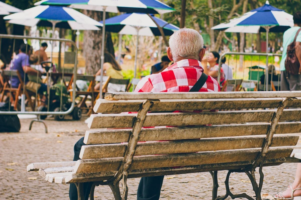 Senhor idoso sentado num banco de praça, no Brasil