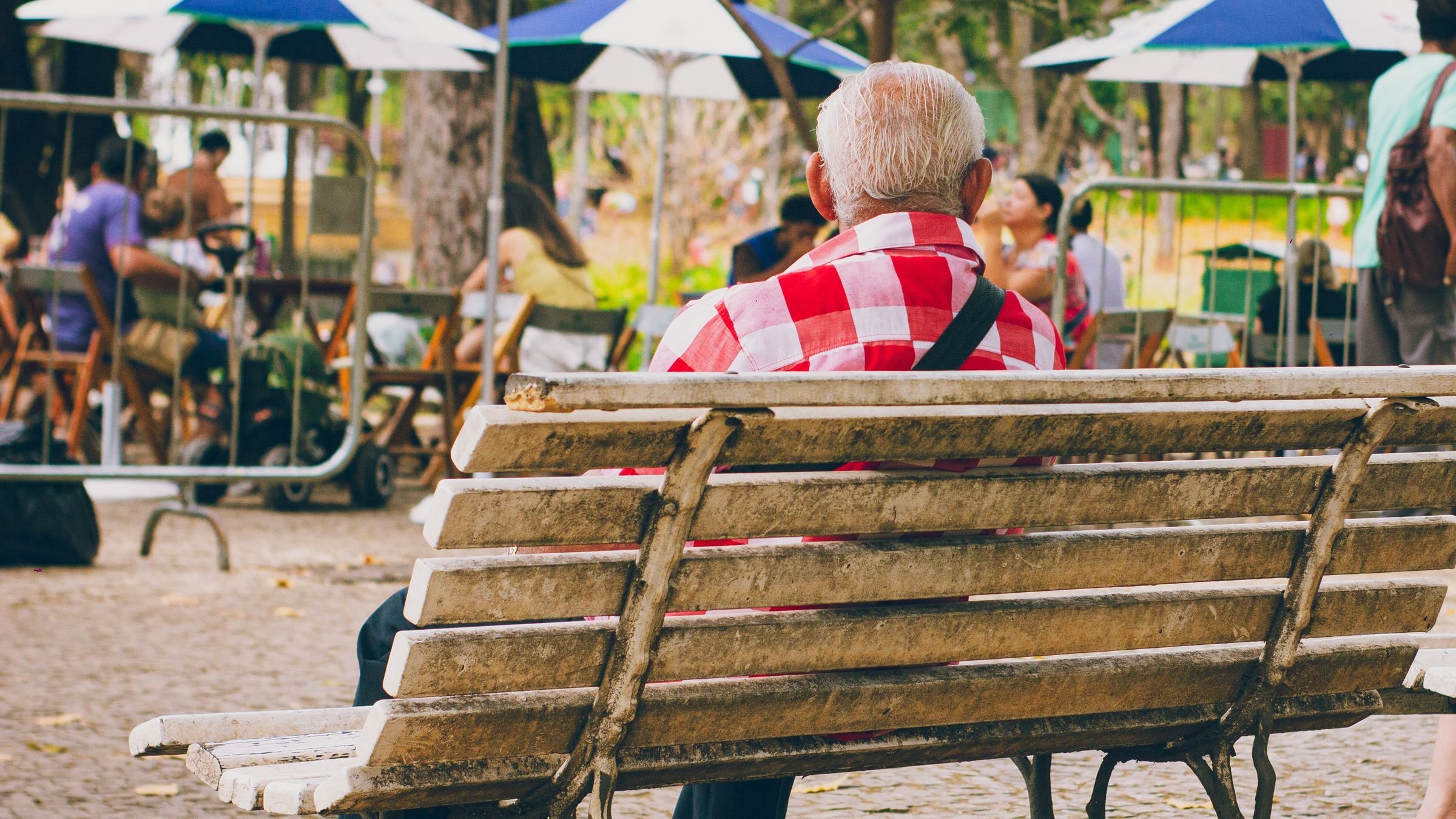 Senhor idoso sentado num banco de praça, no Brasil