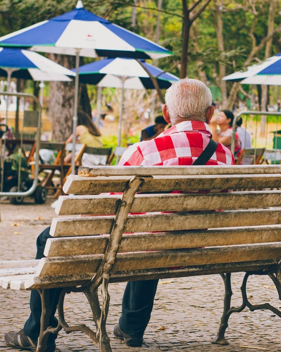 Senhor idoso sentado num banco de praça